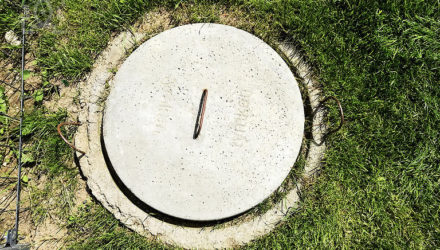 Zbiornik bezodpływowy - na zdjęciu betonowa okrągła klapa zakrywająca otwór szamba, otoczona przez zieloną trawę